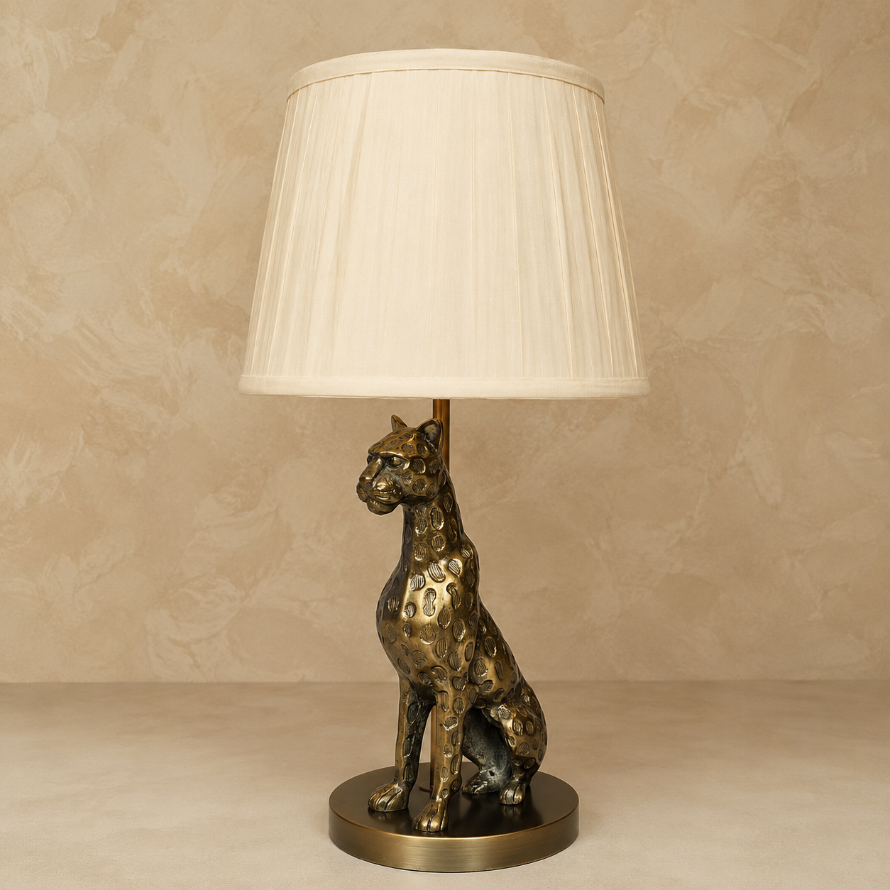 Antique brass leopard table lamp with a white pleated fabric lampshade on a neutral beige background by Inara Home Decor.