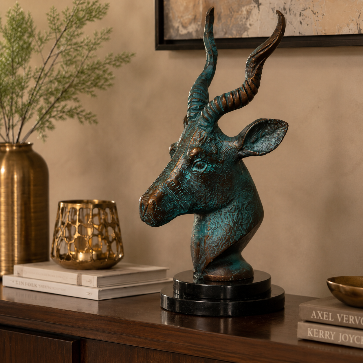 Luxury antelope head sculpture with verdigris patina displayed on a walnut console table alongside decorative books, a gold candle holder, and a brass vase, creating an elegant modern home décor setting.