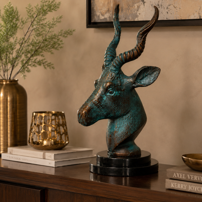 Luxury antelope head sculpture with verdigris patina displayed on a walnut console table alongside decorative books, a gold candle holder, and a brass vase, creating an elegant modern home décor setting.