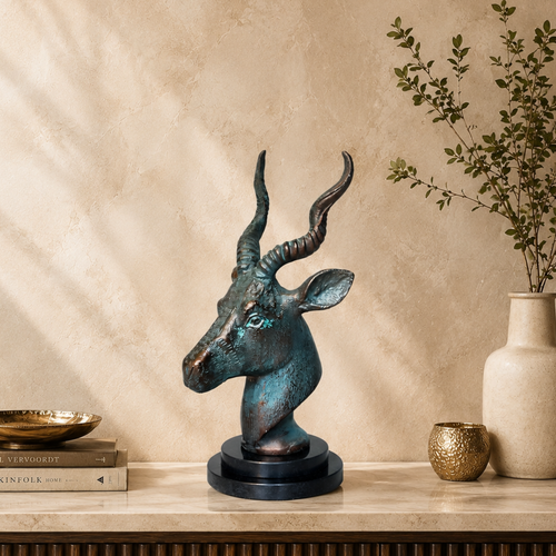 Luxury antique bronze antelope head sculpture displayed on a premium fluted console against a warm beige Venetian plaster wall with natural light, styled with designer books, a ceramic vase, and elegant home décor accessories.