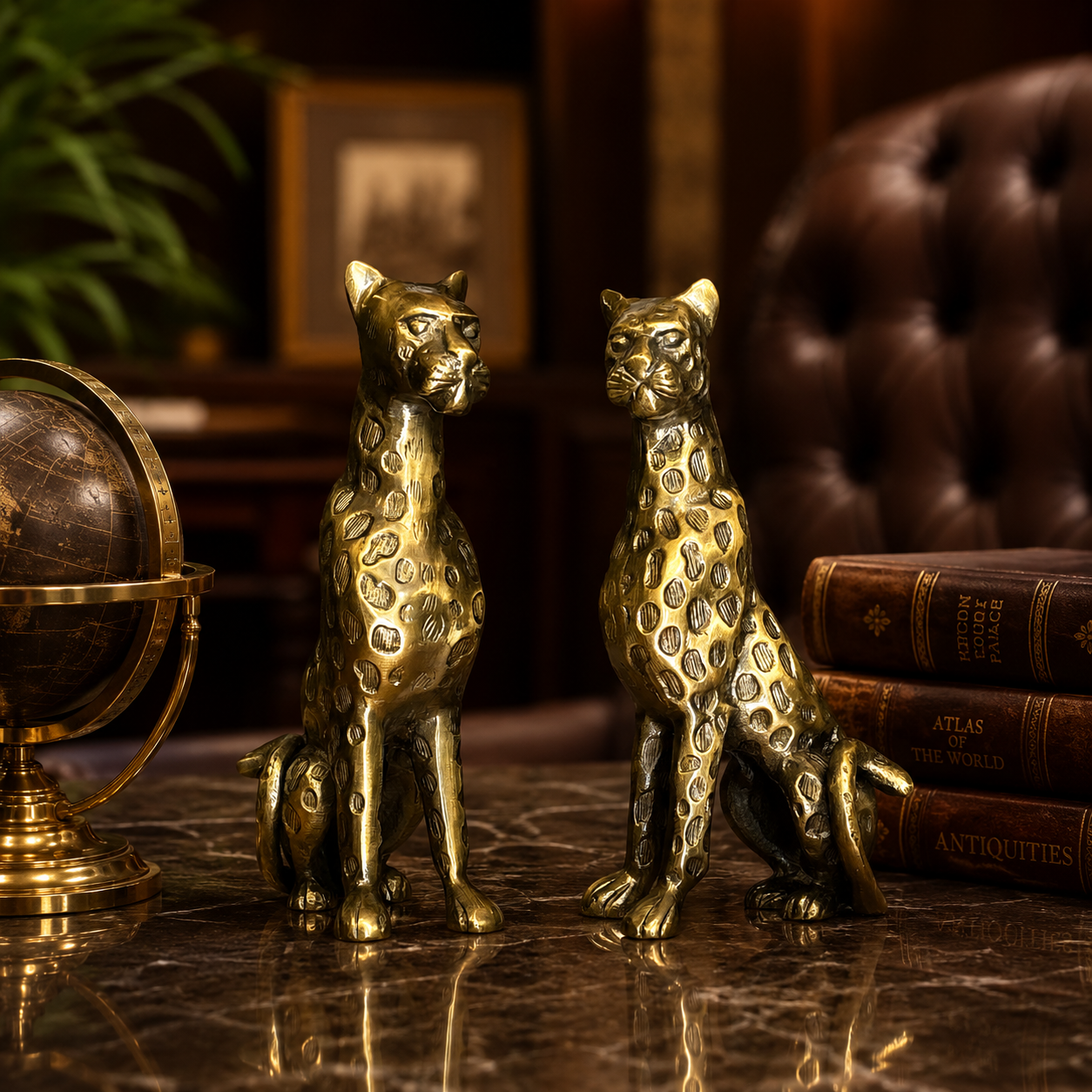 Pair of luxury gold cheetah sculptures displayed on a polished marble console table with vintage leather-bound books and a brass globe in an elegant high-end study interior.