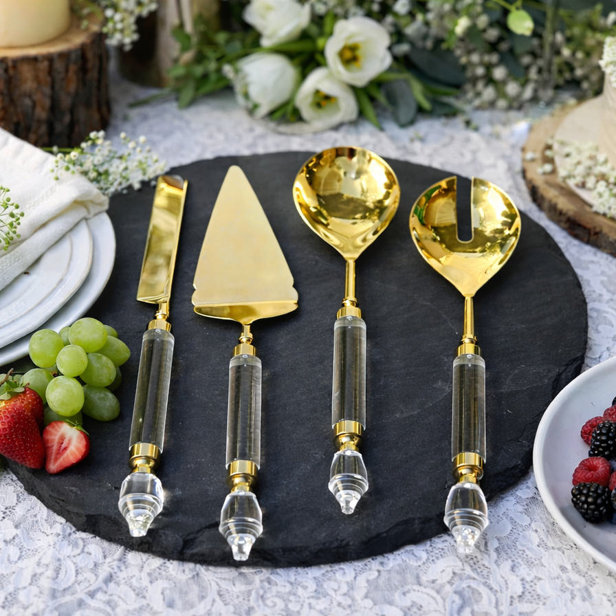 Luxury gold serving cutlery set with crystal handles styled on a dark black slate platter, featuring a cake server, knife, solid spoon and slotted spoon in an elegant tablescape setting.