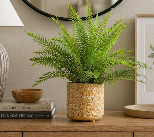 hand-painted yellow ceramic planter with an embossed leaf pattern sitting on a wooden console table next to books and a green fern