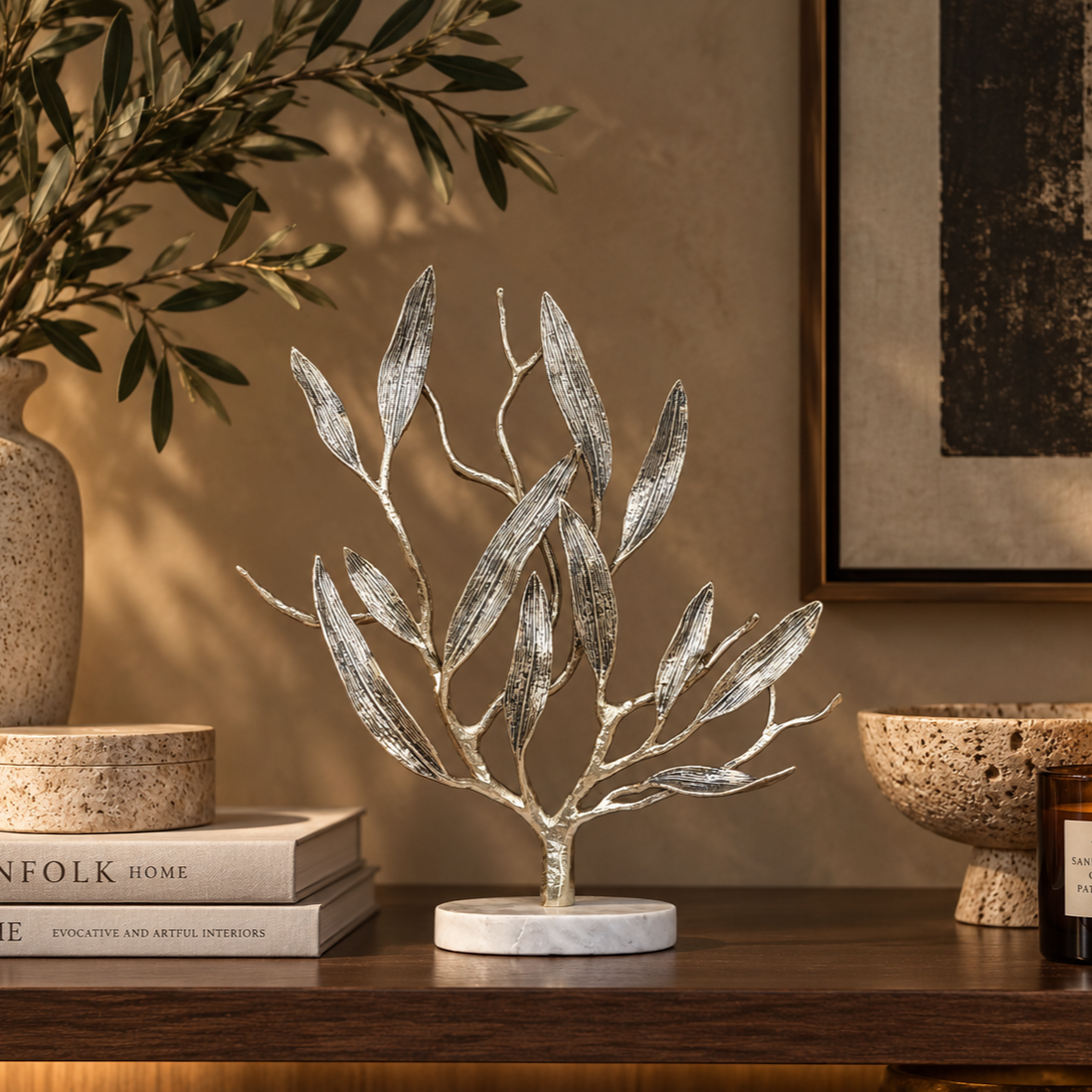 Luxury metal olive tree sculpture styled on a wooden console with designer books and premium home décor accessories in a modern interior.