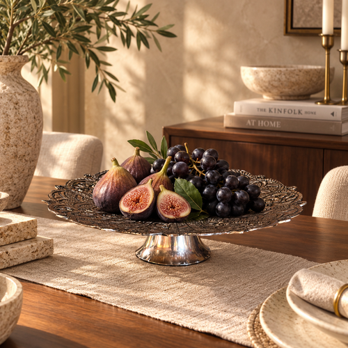 Decorative metal pedestal serving stand displaying fresh figs and grapes on a luxury dining table in a modern home interior.
