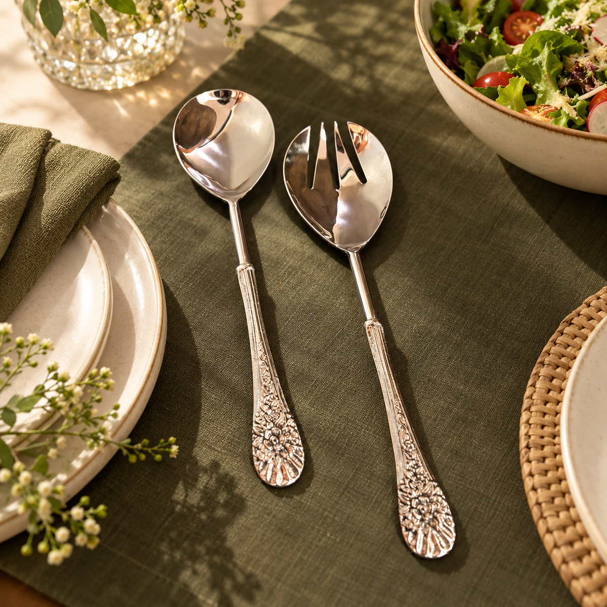 Luxury stainless steel floral salad server spoon and fork set styled on an elegant dining table with olive green linen, ceramic plates and a fresh salad in a premium dining room setting.