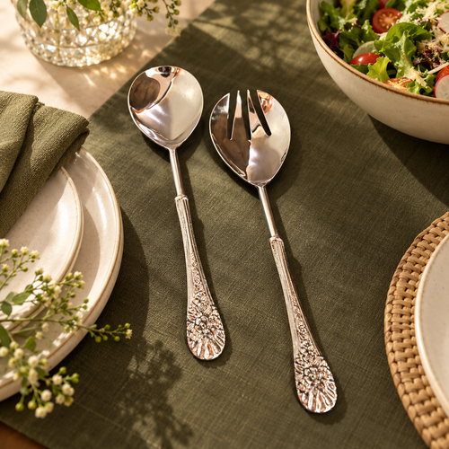 Luxury stainless steel floral salad server spoon and fork set styled on an elegant dining table with olive green linen, ceramic plates and a fresh salad in a premium dining room setting.