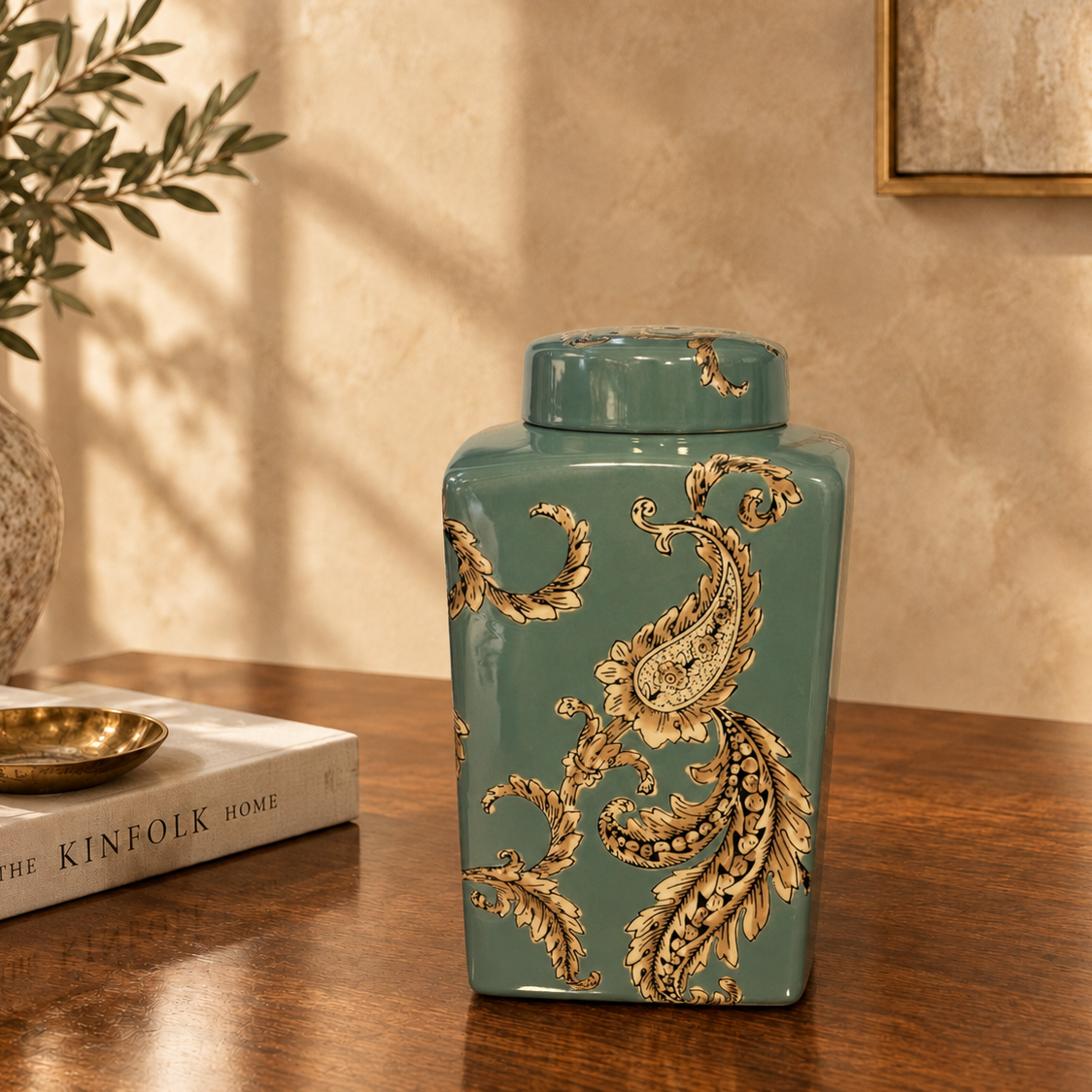 Luxury teal ceramic decorative jar with ornate gold paisley detailing displayed on a dark walnut console table in an elegant modern living room setting by Inara Home Decor.