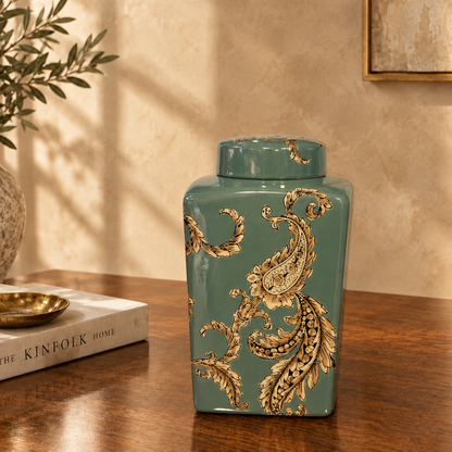 Luxury teal ceramic decorative jar with ornate gold paisley detailing displayed on a dark walnut console table in an elegant modern living room setting by Inara Home Decor.