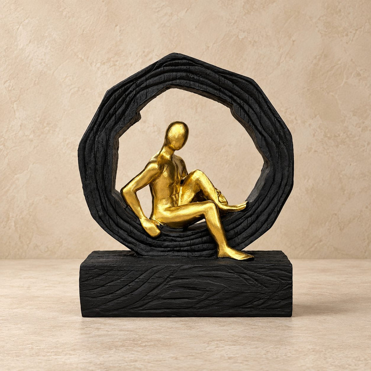 Modern abstract resin sculpture featuring a gold seated figure inside a textured black circular frame on a neutral background.