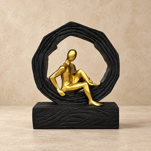 Modern abstract resin sculpture featuring a gold seated figure inside a textured black circular frame on a neutral background.