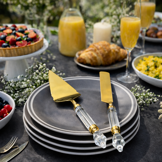 Modern gold cake server and knife set with clear acrylic handles placed on grey ceramic plates in a luxury brunch table setting