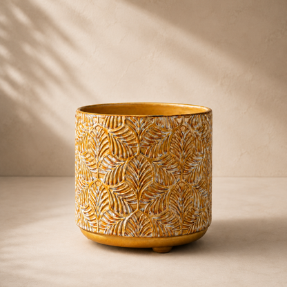 Front view of a handcrafted mustard yellow embossed ceramic planter with raised leaf texture on a warm beige background.