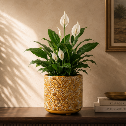 Mustard yellow embossed ceramic planter with leaf texture holding a Peace Lily, styled on a wooden console in a luxury living room.