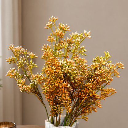 Close-up lifestyle image of orange artificial flower stems arranged in a modern white textured ceramic vase on a wooden table against a soft beige wall background.