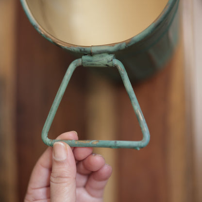 Close-up of the handcrafted triangular side handle on a vintage patina ribbed metal planter with distressed finish.