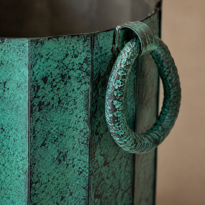 Macro close-up of the textured antique green finish and handcrafted ring handle on a decorative metal planter for indoor home décor.