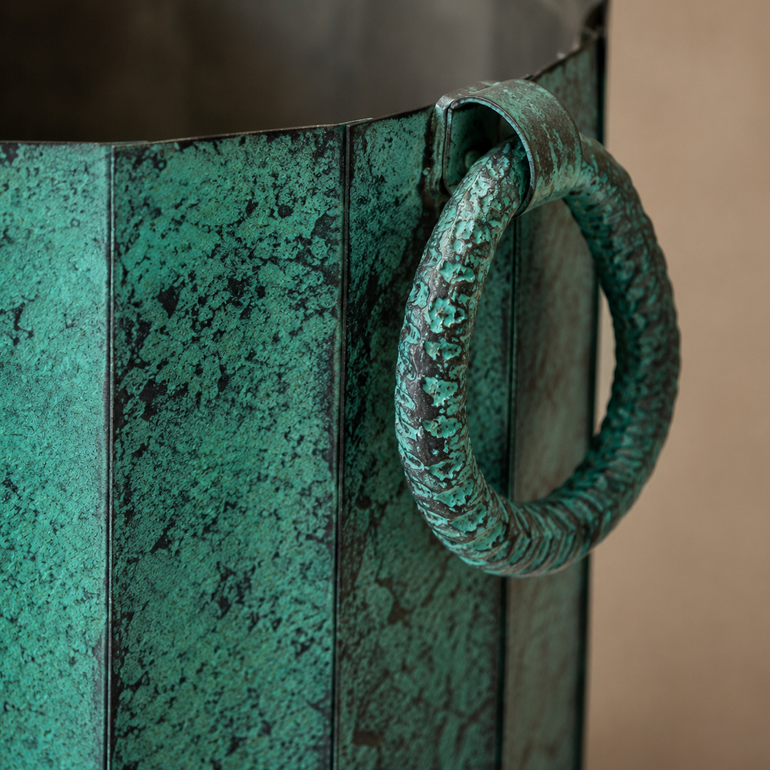 Macro close-up of the textured antique green finish and handcrafted ring handle on a decorative metal planter for indoor home décor.