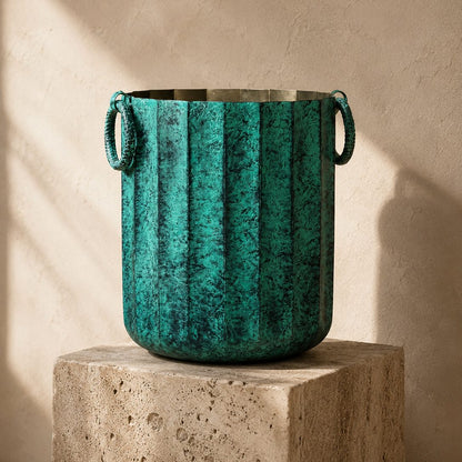 Vintage green metal planter with decorative ring handles displayed on a travertine pedestal featuring an antique textured finish for luxury home décor.