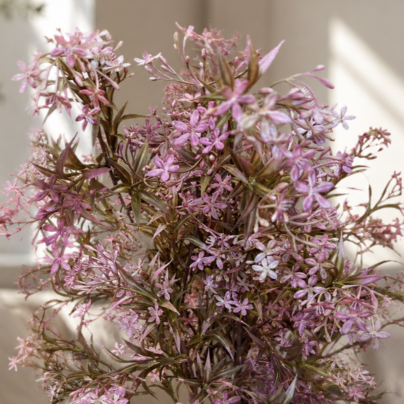 Close-up lifestyle view of a pink artificial wildflower bouquet arranged in a textured ceramic vase, styled on a coffee table in a bright, elegant living room with soft natural light.