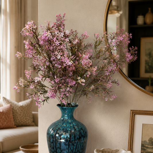 Elegant pink wildflower arrangement in a textured blue glass vase displayed on a wooden console table in a modern luxury living room with soft natural lighting.