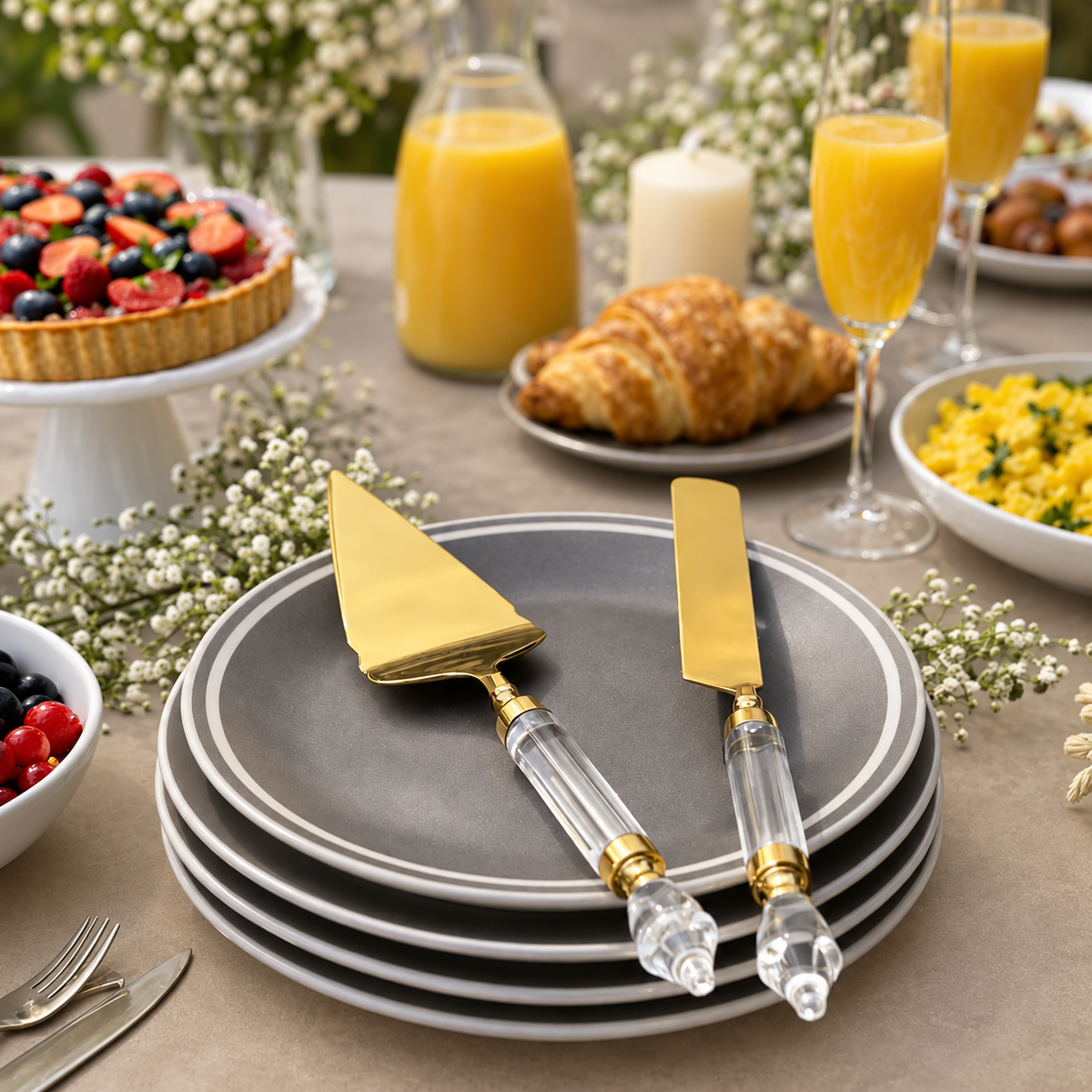 Premium Gold Cake Server & Knife Set with Clear Acrylic Handles displayed on elegant grey dinner plates in a luxury brunch table setting with fruit tart, croissants and orange juice.