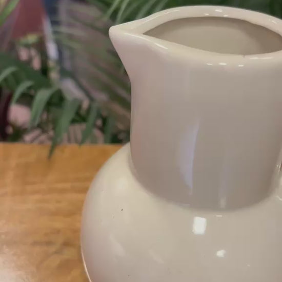 Video showcasing the detailed craftsmanship of a white ceramic pitcher vase with a sculpted loop handle, styled in a warm rustic kitchen-inspired setting.