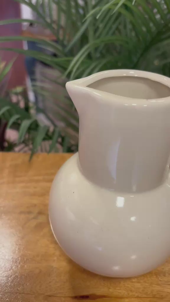 Video showcasing the detailed craftsmanship of a white ceramic pitcher vase with a sculpted loop handle, styled in a warm rustic kitchen-inspired setting.