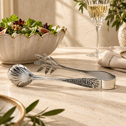 Premium handcrafted silver salad serving tongs with decorative engraved handles and polished stainless steel finish, elegantly showcased in a luxury dining setting while serving fresh salad. A timeless serving accessory for sophisticated table settings by Inara Home Decor.