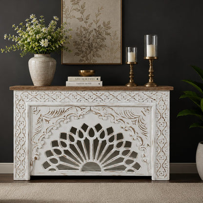 Handcrafted distressed white wooden console table with intricate floral carvings and a natural wood top, styled in a luxury living room against a dark wall.