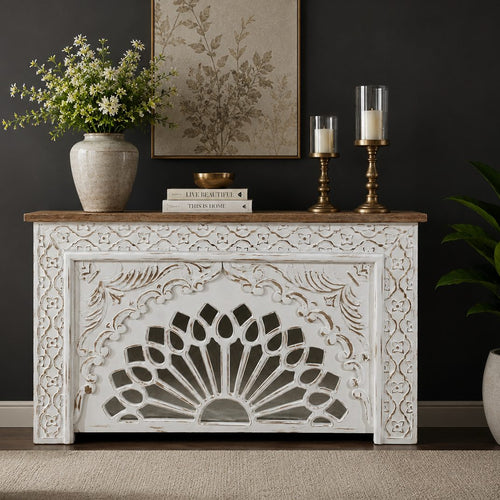 Handcrafted distressed white wooden console table with intricate floral carvings and a natural wood top, styled in a luxury living room against a dark wall.