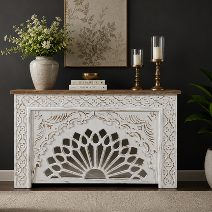 Handcrafted distressed white wooden console table with intricate floral carvings and a natural wood top, styled in a luxury living room against a dark wall.