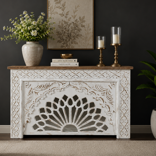 Handcrafted distressed white wooden console table with intricate floral carvings and a natural wood top, styled in a luxury living room against a dark wall.
