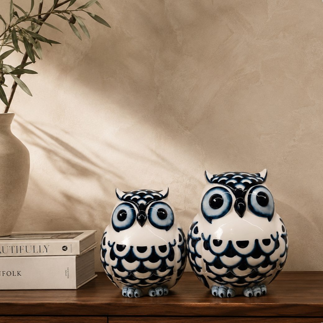 Blue and white ceramic owl figurines displayed on a premium walnut console table with luxury coffee table books, an elegant ceramic vase, and an olive branch against a warm beige Venetian plaster wall. Perfect decorative owl sculptures for sophisticated home décor.