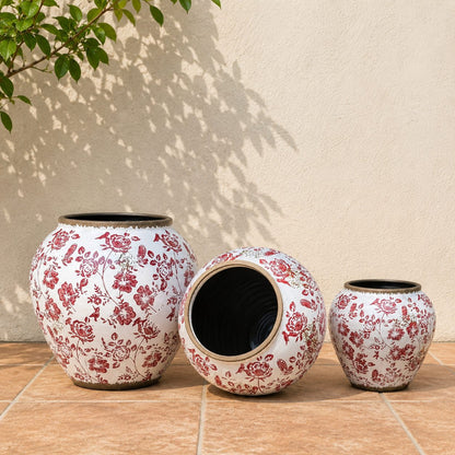 Lifestyle image of red floral ceramic planters with vintage botanical patterns placed against a neutral wall in a sunlit outdoor setting.