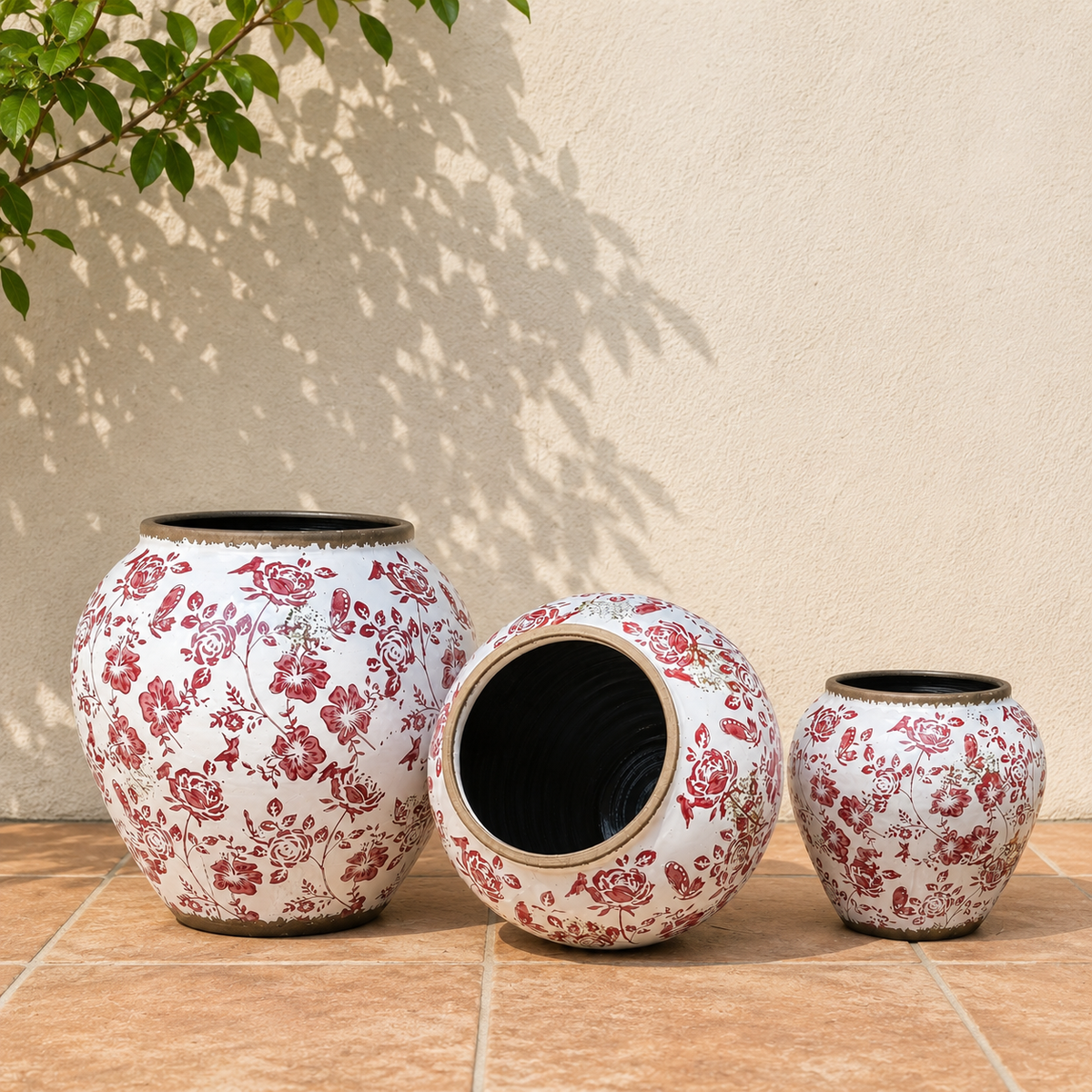 Lifestyle image of red floral ceramic planters with vintage botanical patterns placed against a neutral wall in a sunlit outdoor setting.