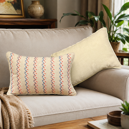 Beige embroidered lumbar cushion cover with red and blue zigzag pattern styled on a neutral sofa in a modern living room by Inara Home Decor.
