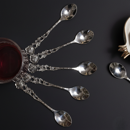 A creative radial arrangement of silver dessert spoons with rose handles fanning out from a tea glass against a minimalist matte black background.