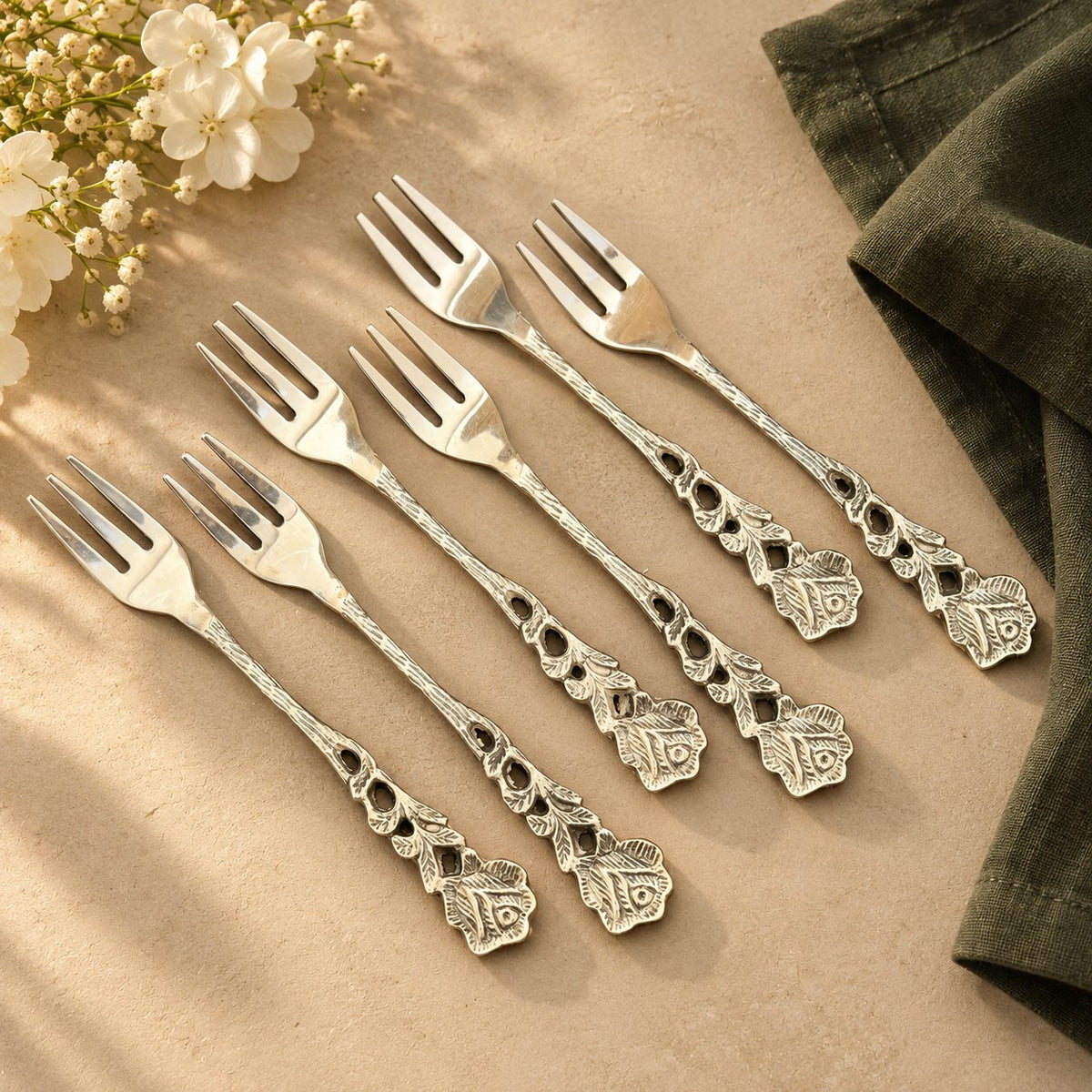 Set of six rose fruit forks with ornate floral handles arranged on a beige stone surface.