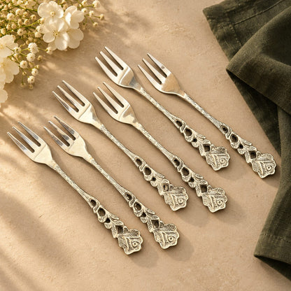 Set of six rose fruit forks with ornate floral handles arranged on a beige stone surface.