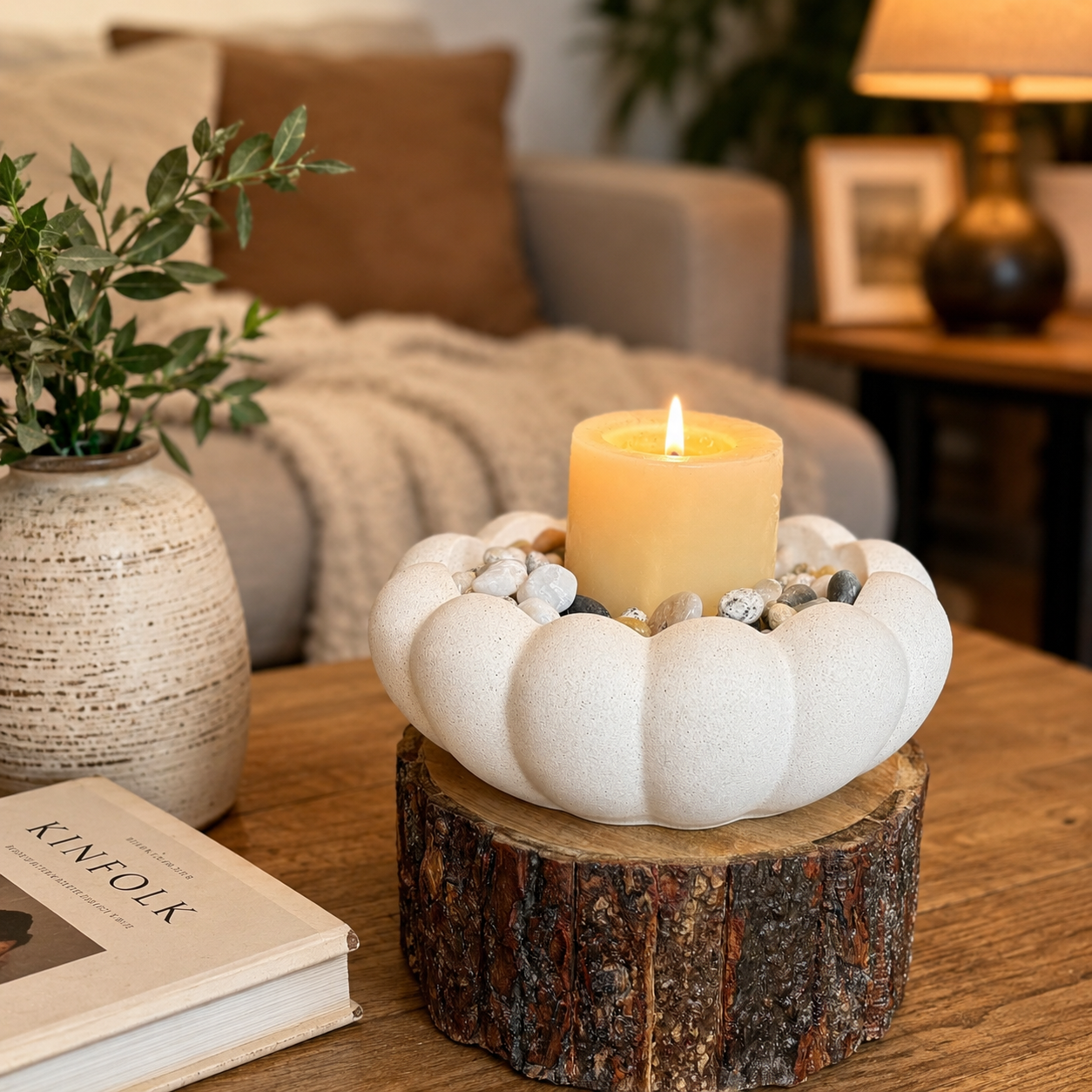 Rustic ceramic pebble candle holder with a lit candle on a wooden bark base, styled on a cozy living room coffee table with warm decor accents.