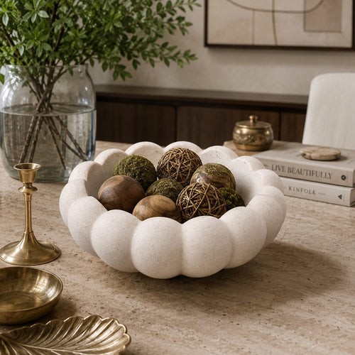 White scalloped ceramic decorative bowl styled on a luxury console table with decorative spheres in a modern contemporary home interior.