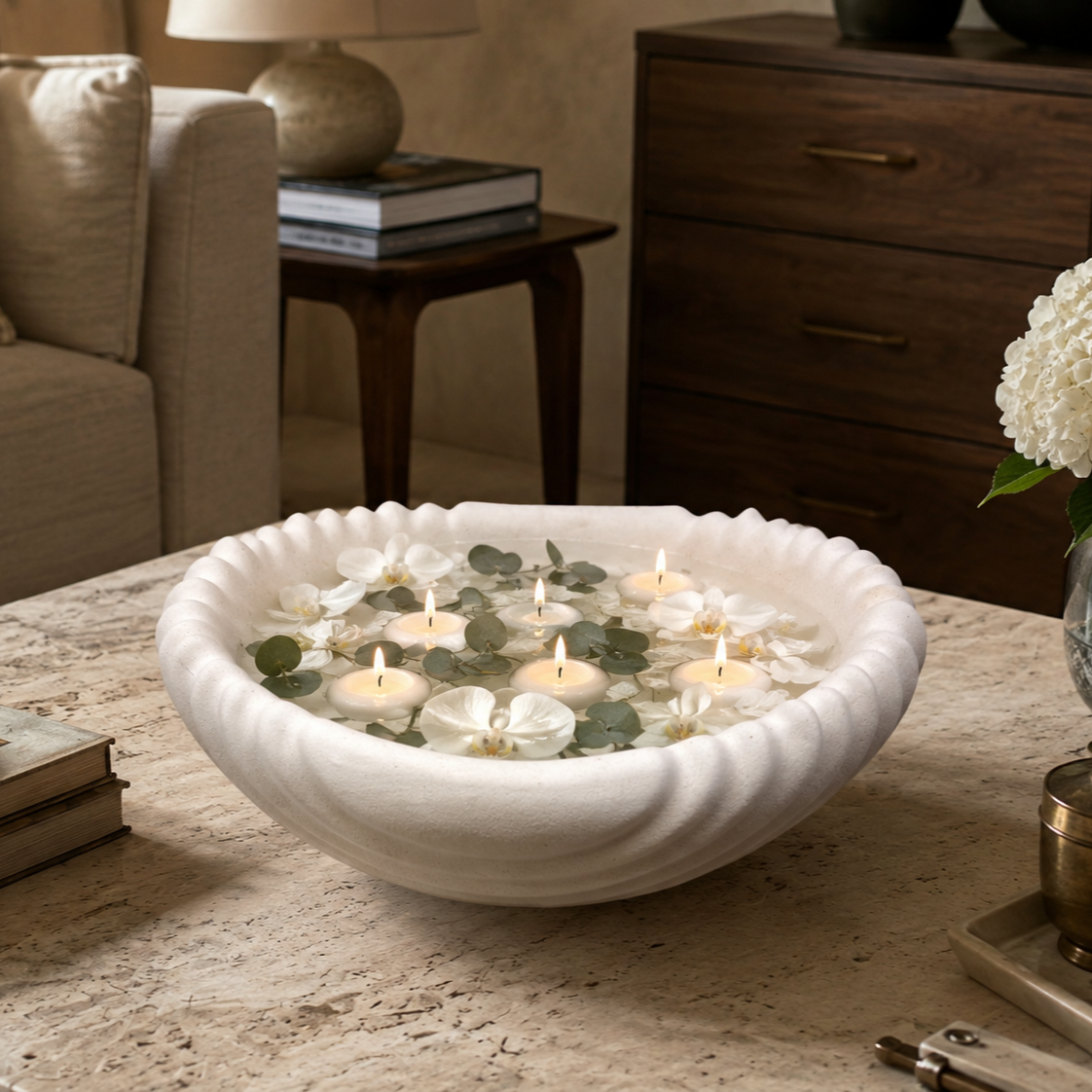 Scalloped white ceramic urli filled with floating candles, white orchids, and eucalyptus leaves, creating an elegant coffee table centerpiece.
