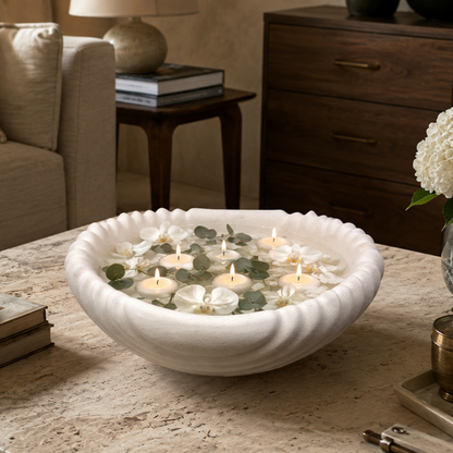 Scalloped white ceramic urli filled with floating candles, white orchids, and eucalyptus leaves, creating an elegant coffee table centerpiece.