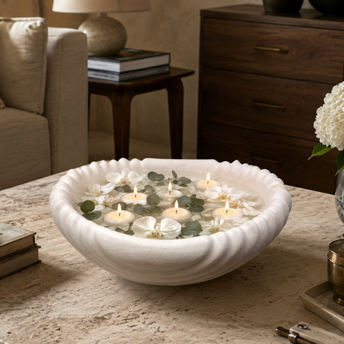 Scalloped white ceramic urli filled with floating candles, white orchids, and eucalyptus leaves, creating an elegant coffee table centerpiece.