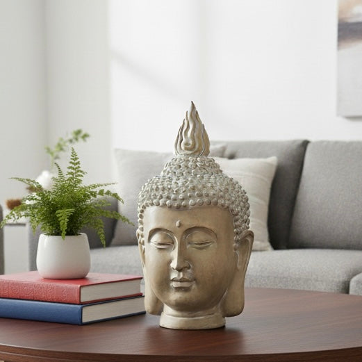 A premium stone-finish Buddha head sculpture placed on a wooden coffee table next to books and a potted fern in a modern living room setting.