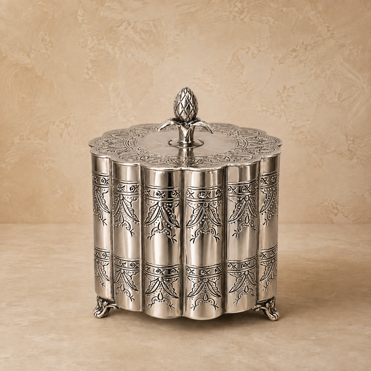 Silver engraved metal storage container with decorative lid and ornate feet on a warm beige studio background, luxury handcrafted home décor accent for elegant interiors.