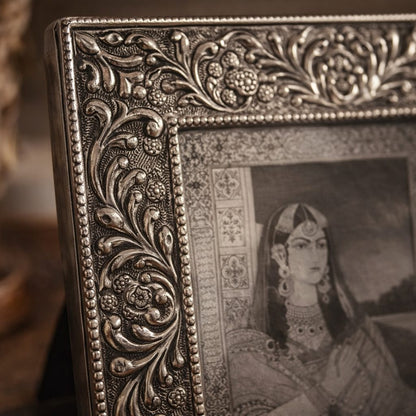 Close-up of an ornate antique silver photo frame with intricate floral embossing, featuring a vintage Indian royal portrait, styled in a warm luxury home décor setting.