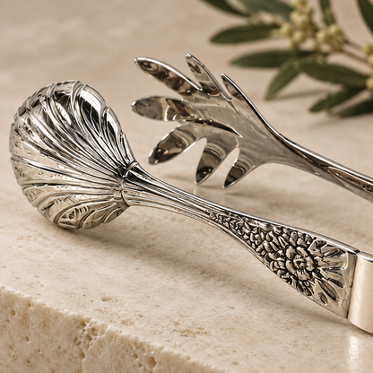 Close-up of handcrafted silver salad serving tongs showcasing decorative floral engraving and polished stainless steel finish.