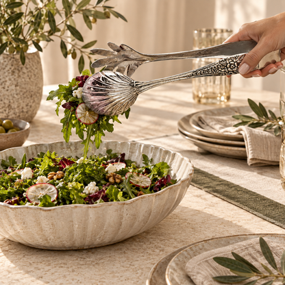Hand using premium silver salad serving tongs to serve fresh garden salad, elegant stainless steel serving accessory for luxury dining.